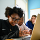 An image from Girls Who Code depicting three young people sitting in front of a macbook, probably coding.